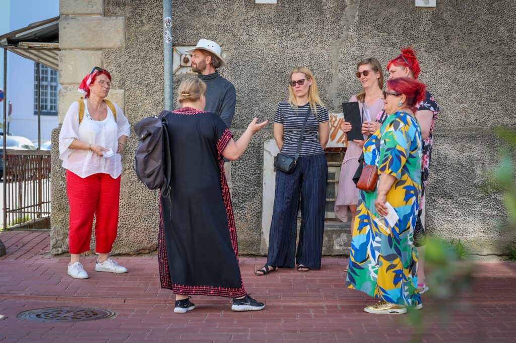 A small group of people listening to a guide during an interactive outdoor history experience in Parnu old town