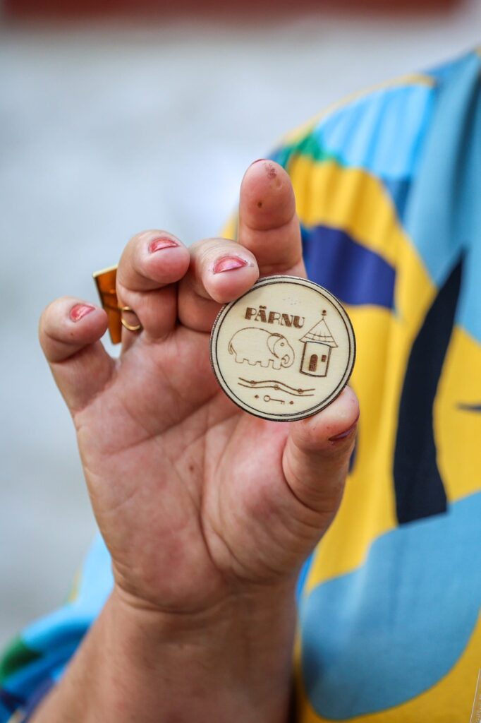 A close-up of a hand holding a custom engraved wooden token souvenir from the Witches and Bitches Parnu walking tour